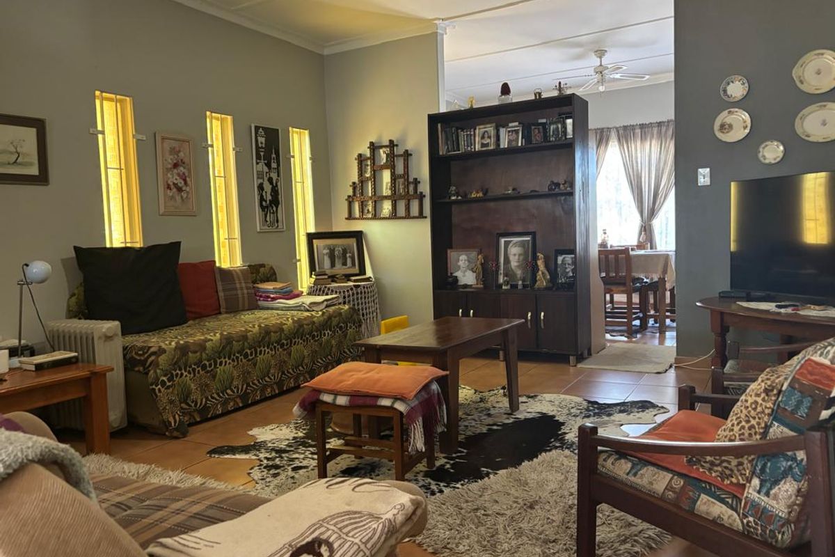 A comfortable living room featuring tiled flooring, vertical windows, and a ceiling fan, with an open-plan flow leading into the adjacent dining area.