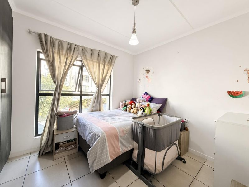 A functional bedroom featuring tiled flooring, a built-in wardrobe, and a large window providing natural light.