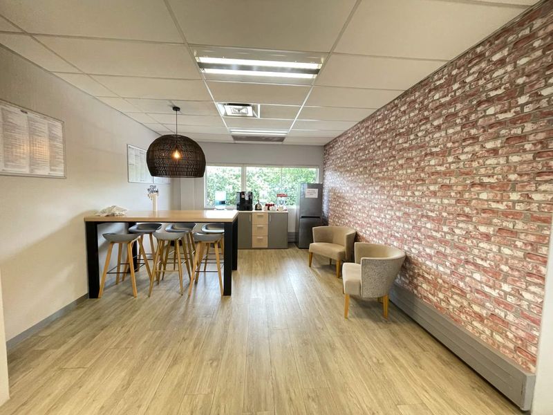 A modern office break area featuring a suspended ceiling, wood-look flooring, and a decorative exposed brick feature wall.