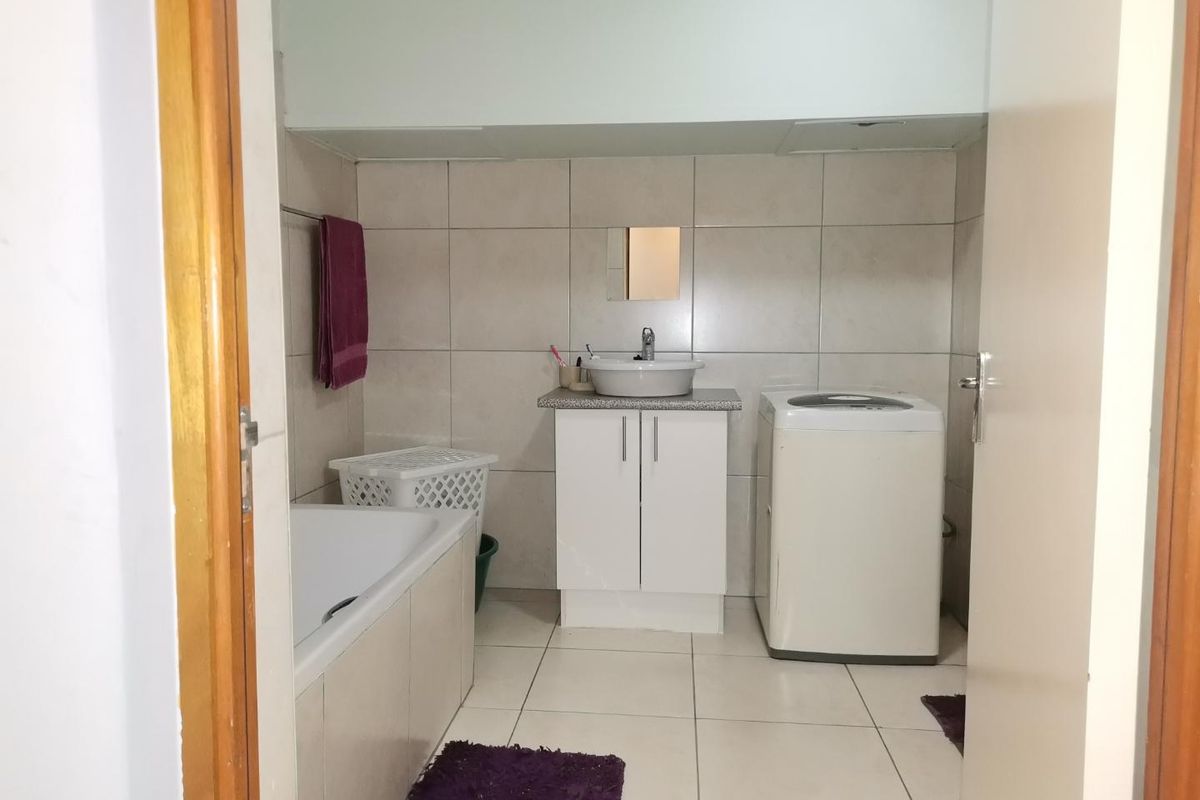 A functional bathroom featuring a built-in bathtub, a vanity cabinet with a basin, and dedicated space for laundry appliances.