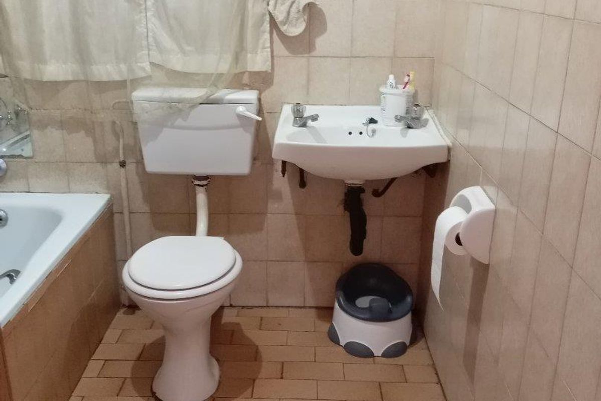 A dated bathroom featuring a standard bathtub, wall-mounted basin, and toilet with ceramic wall and floor tiling.