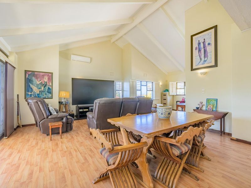 Spacious open-plan living and dining area featuring vaulted ceilings with exposed beams, laminate flooring, and large sliding glass doors providing natural light.