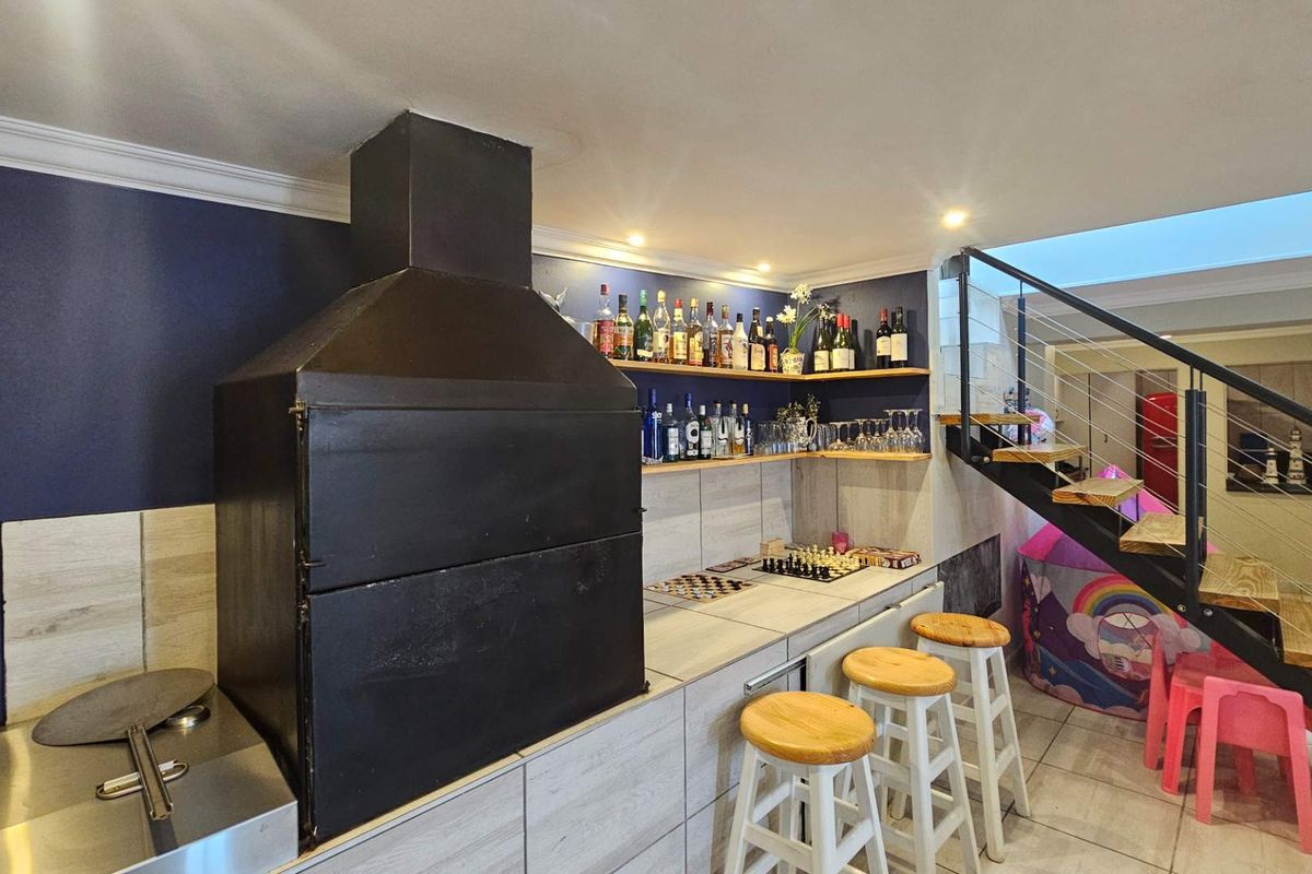 Indoor entertainment area featuring a built-in braai, tiled countertops, open shelving, and a modern staircase with metal railings.