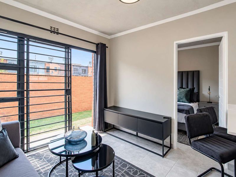 Modern open-plan living area featuring tiled floors, a sliding glass door with security gate, and direct access to an adjacent bedroom.