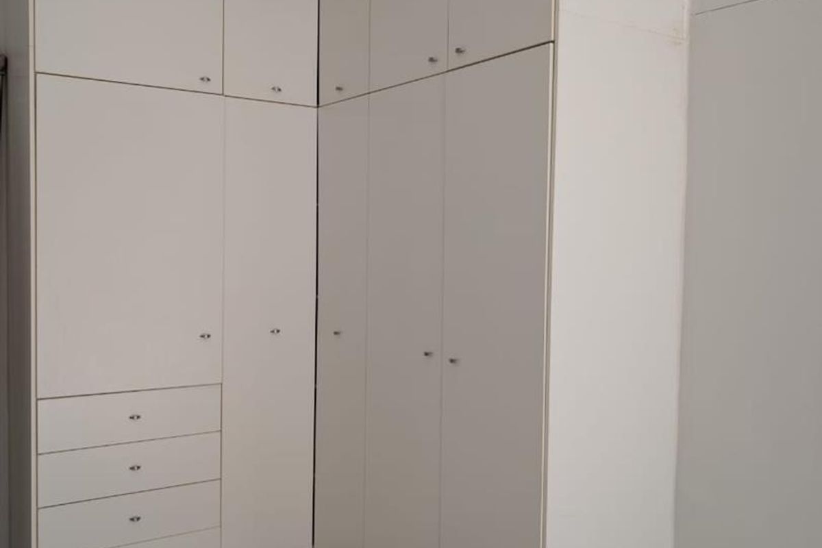 A bedroom featuring floor-to-ceiling built-in white cabinetry with integrated drawers and ample storage space, complemented by neutral tiled flooring.