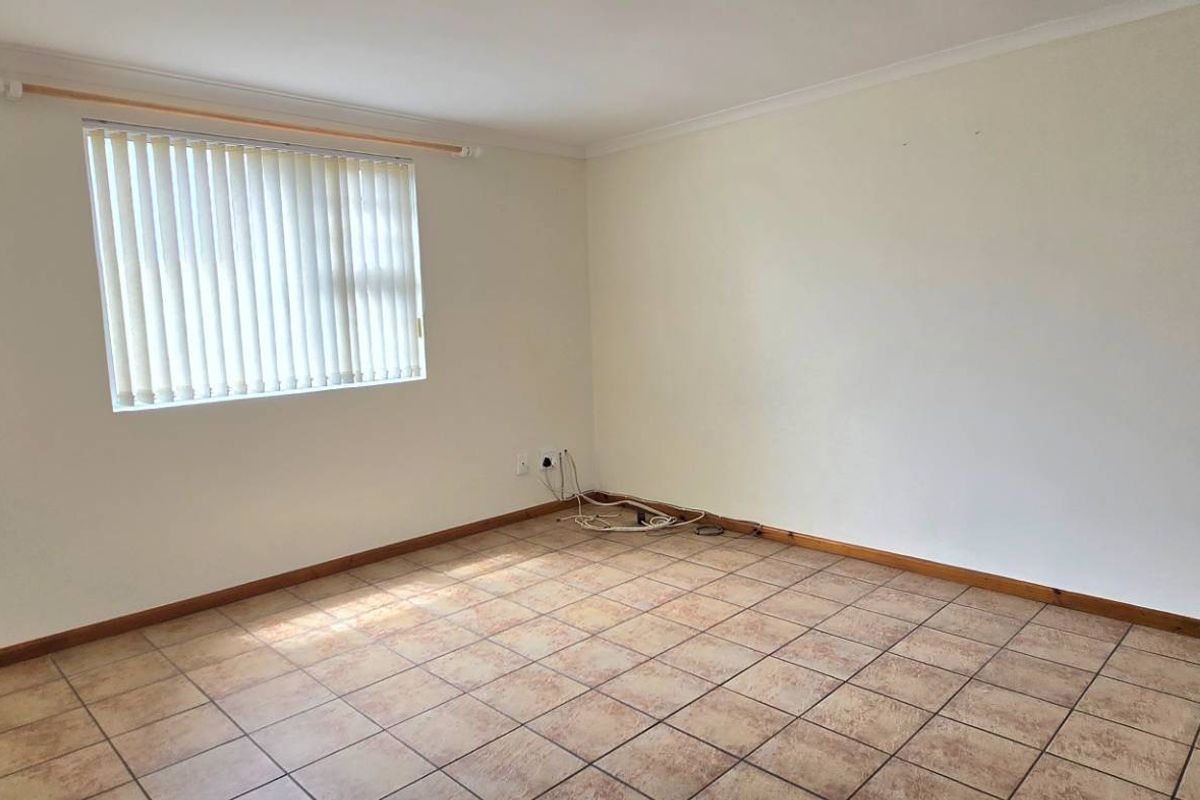 A vacant bedroom featuring neutral wall finishes, tiled flooring, and vertical window blinds.