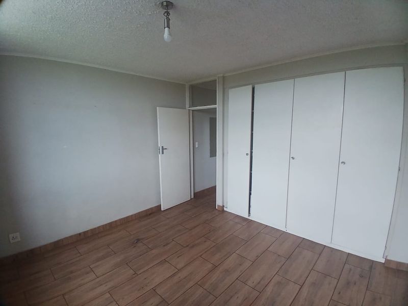 A vacant bedroom featuring wood-look tile flooring, built-in cupboards, and neutral wall finishes, offering a clean canvas for personalization.