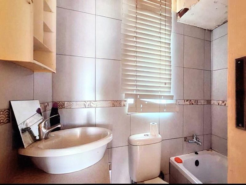 A compact bathroom featuring a vessel sink, toilet, and bathtub with tiled walls. The space requires maintenance and cosmetic updates to improve its condition.
