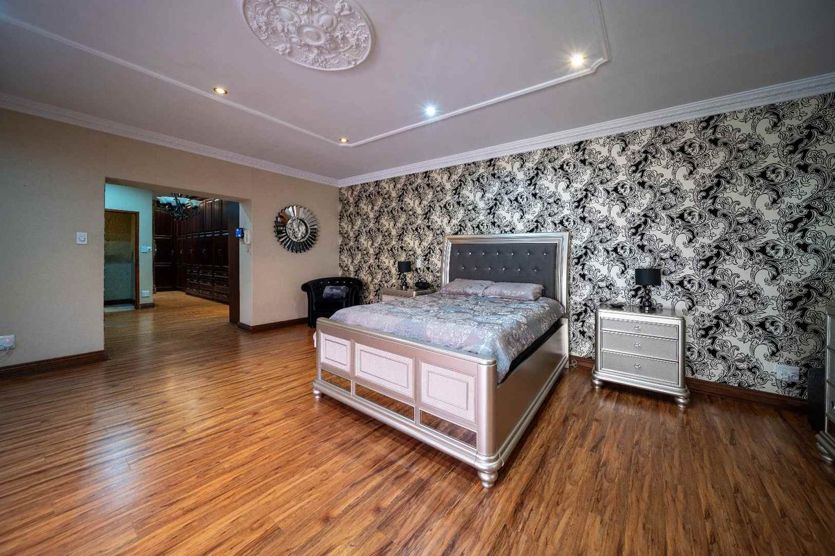 Spacious bedroom featuring laminate wood flooring, decorative ceiling rose, recessed lighting, and a bold patterned feature wall.