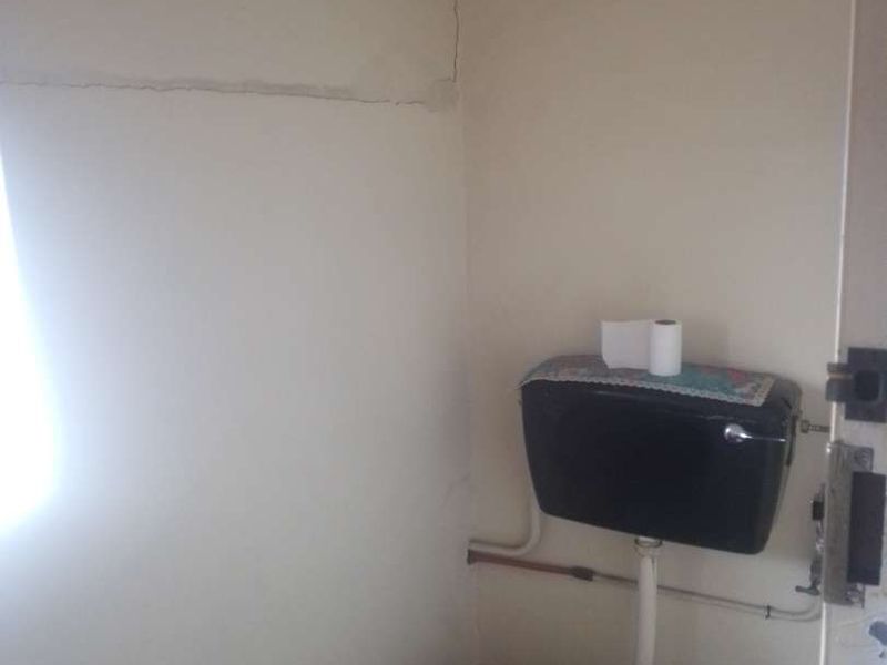 A small bathroom featuring a toilet with a wall-mounted cistern, showing visible cracks in the wall plaster.