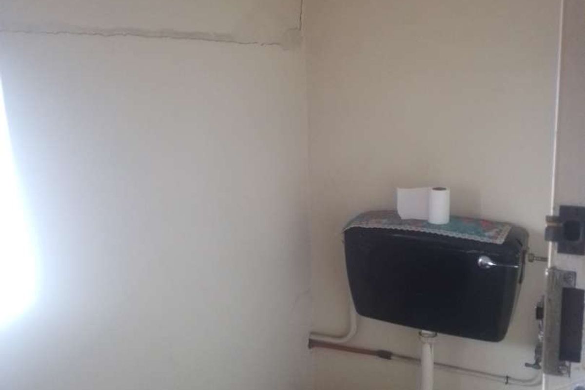 A small bathroom featuring a toilet with a wall-mounted cistern, showing visible cracks in the wall plaster.