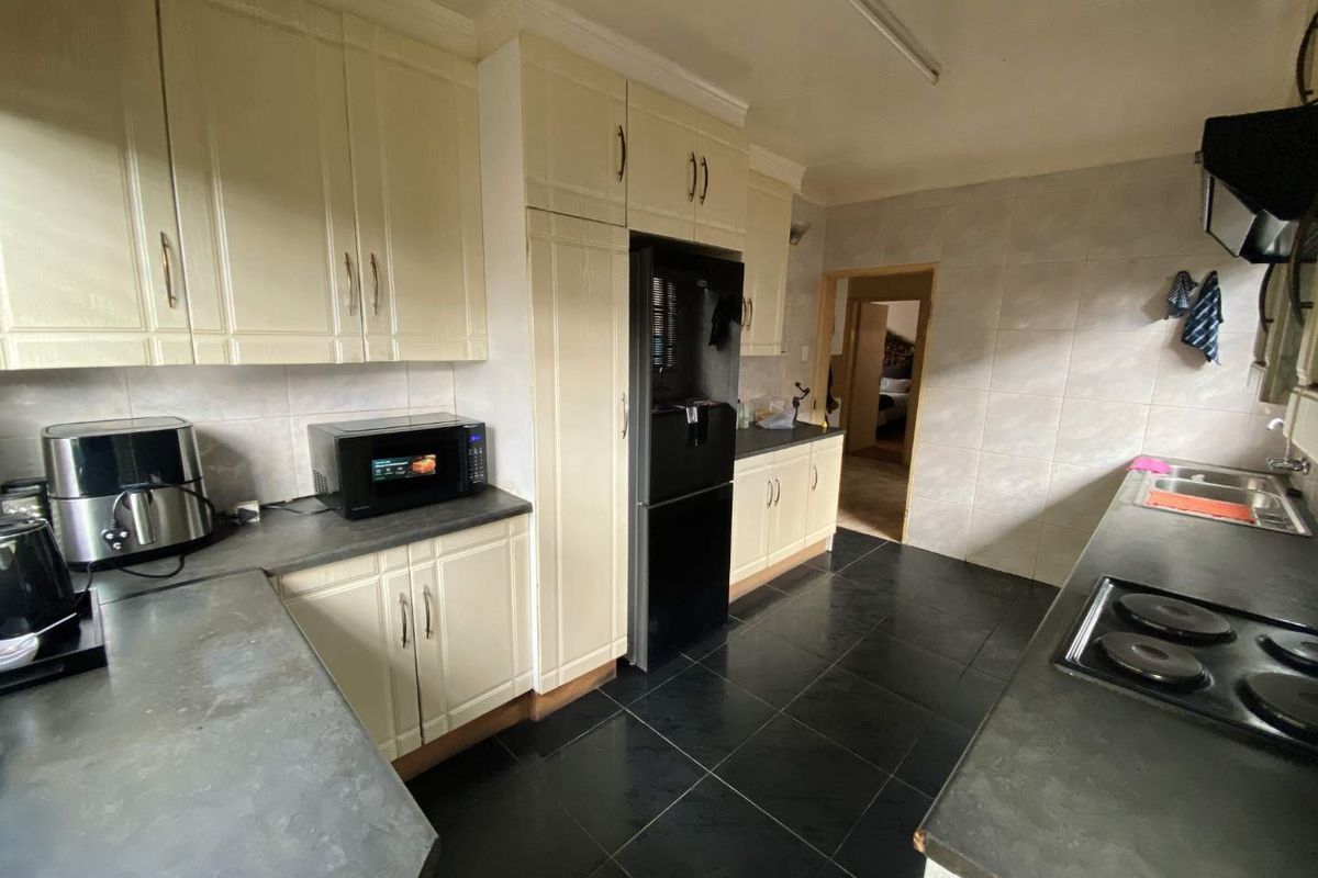 A functional kitchen featuring cream-colored cabinetry, dark countertops, black tiled flooring, and a built-in electric hob with an extractor fan.