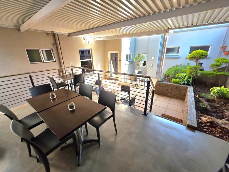 A covered outdoor patio area featuring a concrete floor, metal roofing, and a built-in garden bed, providing a functional space for outdoor seating.