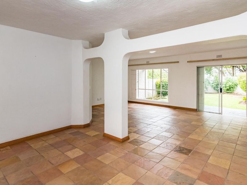 Spacious open-plan living area featuring terracotta tile flooring, distinctive arched architectural detailing, and large sliding glass doors providing access to the rear garden.