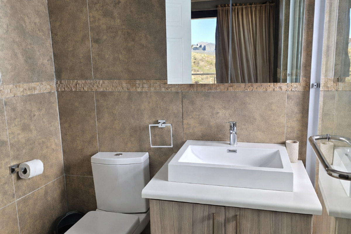 A modern bathroom featuring a vessel sink vanity, wall-mounted mirror cabinet, toilet, and a glass-enclosed shower with neutral earth-toned wall and floor tiles.