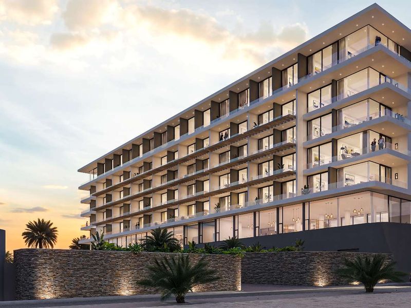 A modern multi-story apartment building featuring glass balconies, stone facade elements, and integrated exterior lighting at dusk.