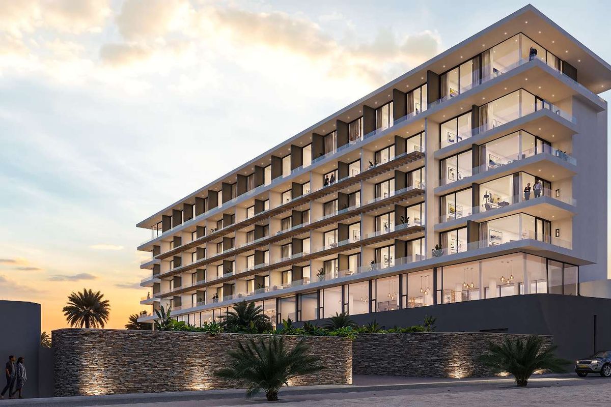 A modern multi-story apartment building featuring glass balconies, stone facade elements, and integrated exterior lighting at dusk.