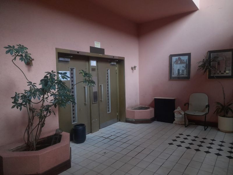 An apartment building entrance lobby featuring double metal doors, tiled flooring, and a built-in planter box.
