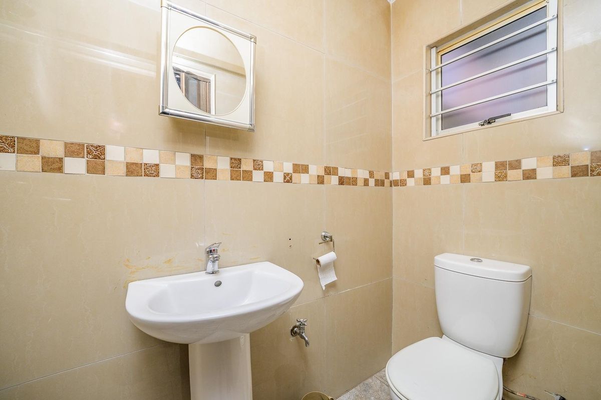 A compact bathroom featuring a pedestal basin, toilet, and neutral wall tiling with a decorative border.