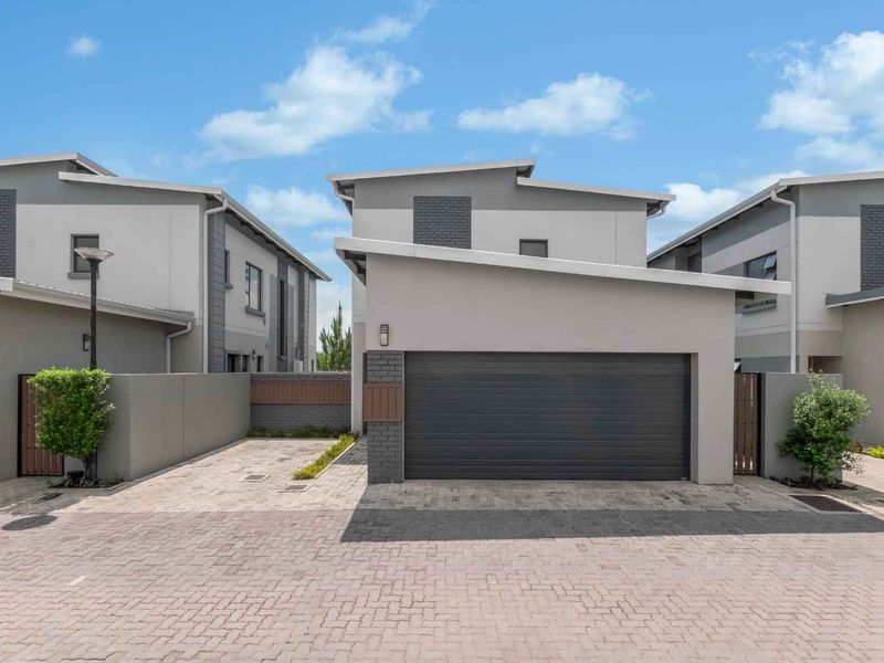 Modern cluster home exterior featuring a paved driveway, secure double garage, and contemporary grey facade with clean architectural lines.