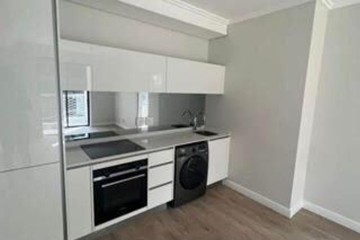 Modern kitchen featuring sleek white cabinetry, integrated oven, electric cooktop, and a mirrored splashback, providing a clean and contemporary aesthetic.