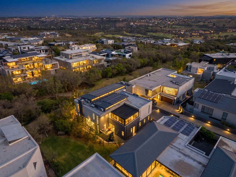 Aerial view of a modern residential property featuring solar panels, a flat roof design, and a landscaped garden within a secure estate setting.