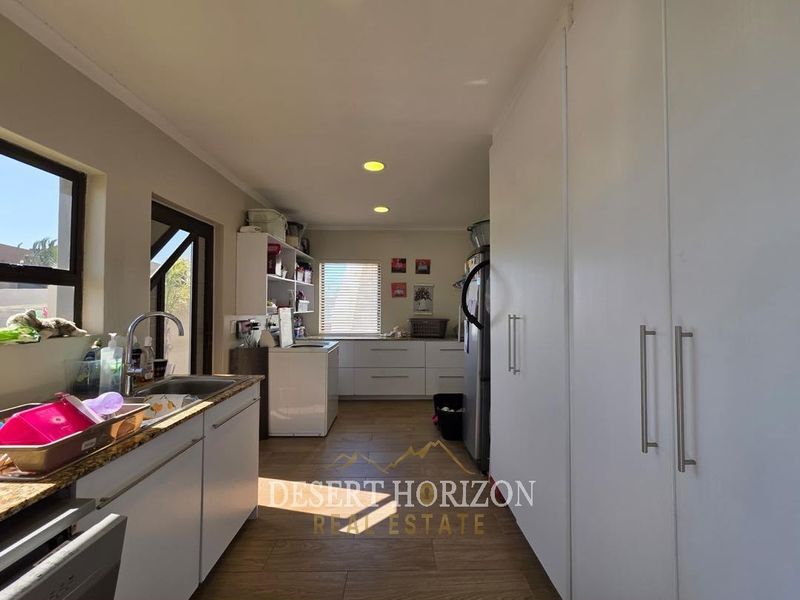 A functional kitchen featuring granite countertops, ample built-in cabinetry, and tiled flooring, offering a practical layout with natural light.