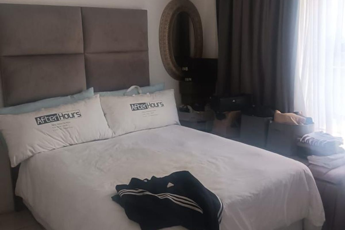 A bedroom featuring a large upholstered headboard and window curtains, providing a functional sleeping space.