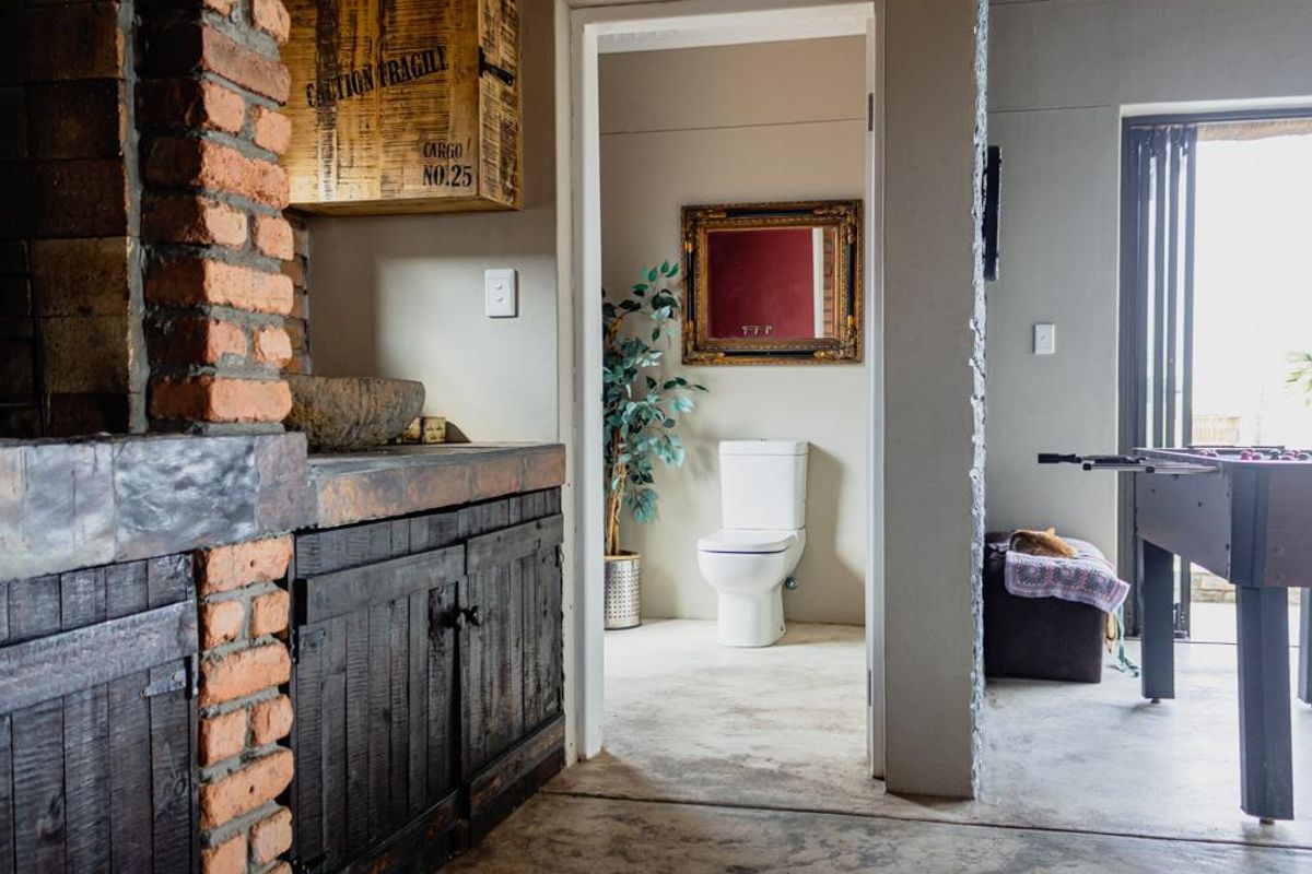 Living area featuring an exposed brick fireplace, rustic built-in cabinetry with a stone basin, and polished concrete flooring, leading to an adjacent bathroom.