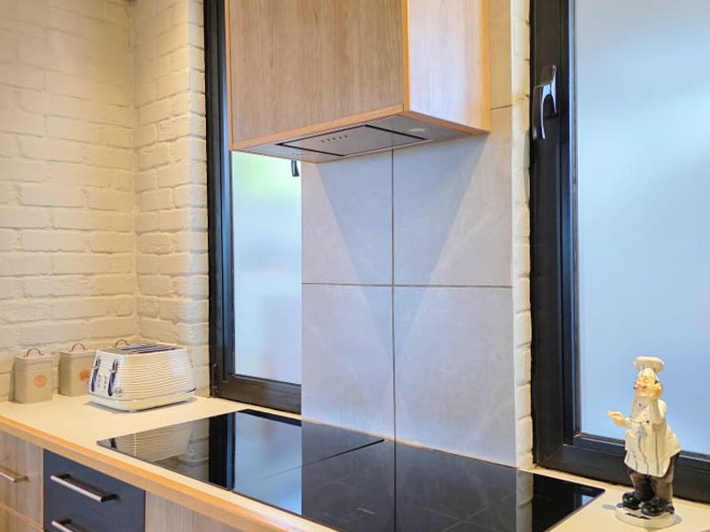 Modern kitchen area featuring a sleek induction cooktop, integrated extractor fan, timber ceiling accents, and contemporary cabinetry with a tiled splashback.
