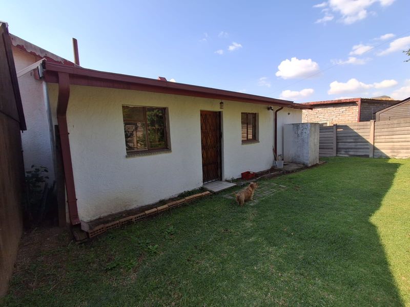 Rear view of the property showing the exterior wall, security gate, and surrounding garden area with precast concrete boundary walling.