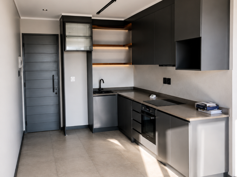 Modern, minimalist kitchen featuring sleek dark grey cabinetry, integrated appliances, open shelving with accent lighting, and neutral tiled flooring.