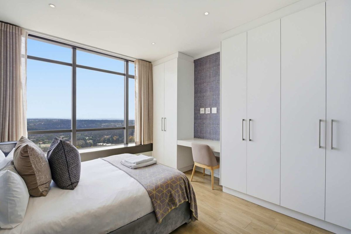 Modern bedroom featuring floor-to-ceiling windows with expansive views, built-in white cabinetry, and a dedicated integrated desk area.