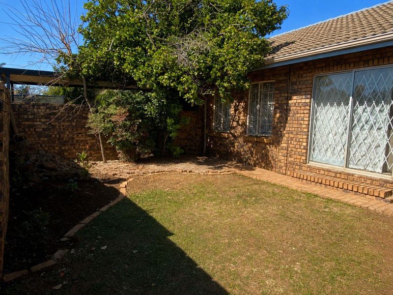 A private rear garden area featuring a face brick townhouse facade, paved pathways, and secure sliding door access.