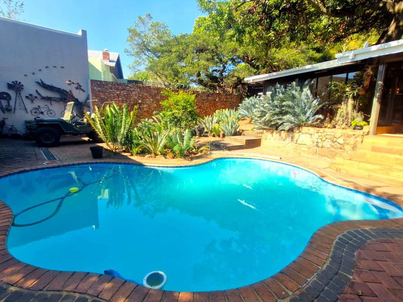 Outdoor pool area featuring a kidney-shaped swimming pool, brick paving, stone retaining walls, and direct access to the home via sliding glass doors.