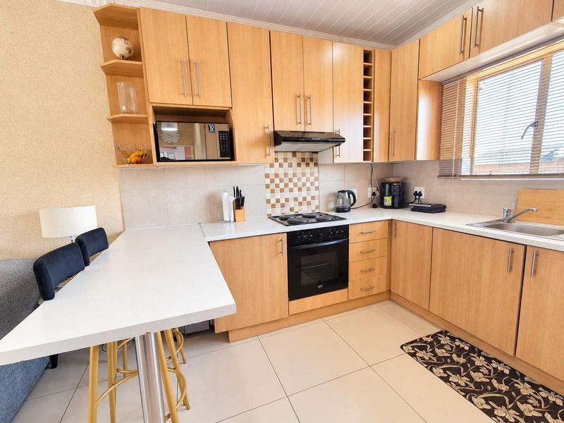 A functional kitchen featuring light wood cabinetry, built-in appliances, a tiled backsplash, and an integrated breakfast bar with tiled flooring.