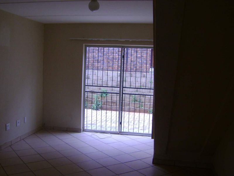 An empty living room featuring tiled flooring and a sliding glass door that opens onto a private paved patio area.