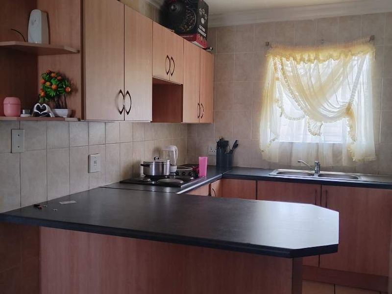 A functional kitchen featuring laminate cabinetry, dark countertops, a built-in hob, and tiled finishes throughout.
