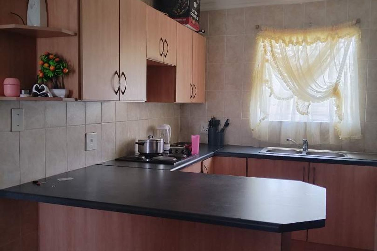 A functional kitchen featuring laminate cabinetry, dark countertops, a built-in hob, and tiled finishes throughout.