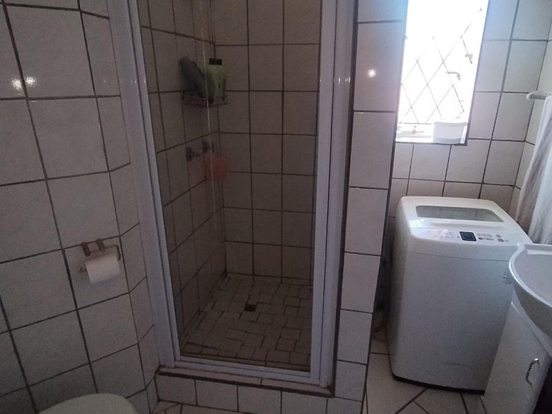 Compact bathroom featuring a shower enclosure, toilet, and vanity basin with tiled finishes throughout.