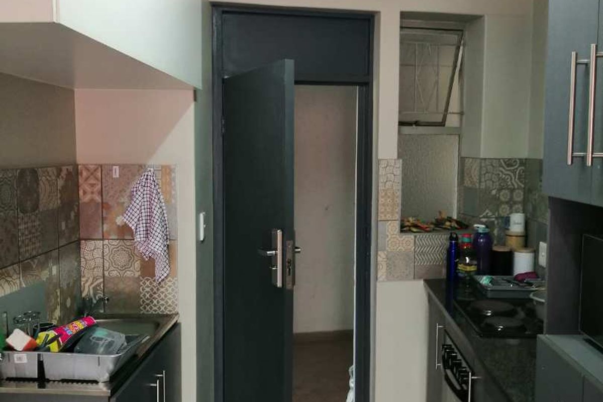 A compact kitchen featuring dark built-in cabinetry, granite countertops, a stainless steel sink, and patterned tiled backsplash.