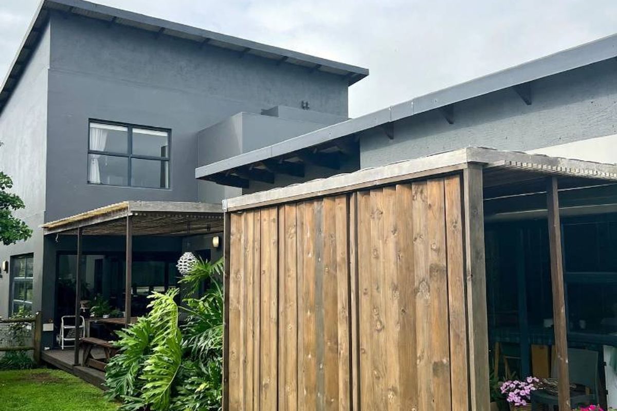 Rear view of the property featuring a timber deck, pergola, and privacy screen overlooking a well-maintained lawn.