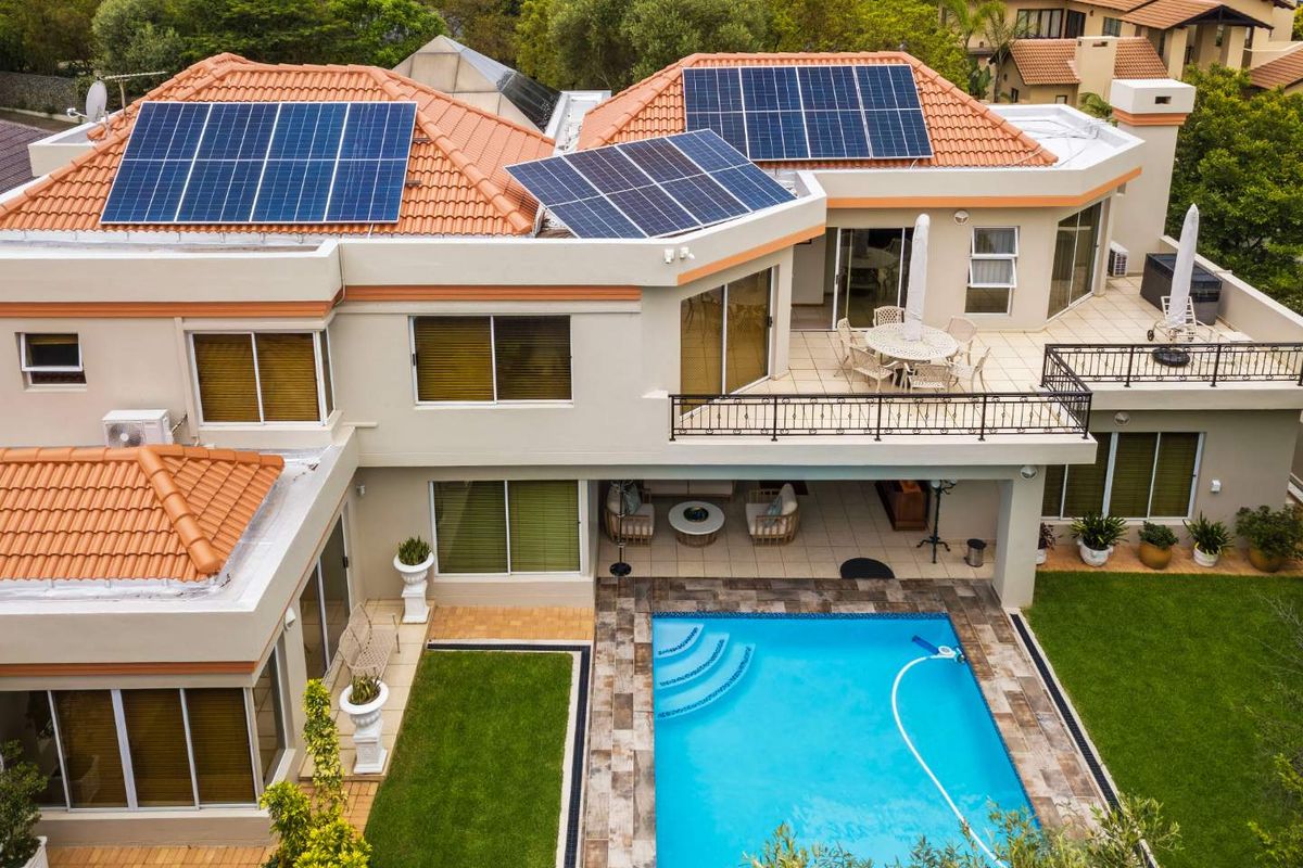 Aerial view of a multi-level residence featuring a tiled roof with solar panels, a swimming pool, a spacious patio, and a landscaped garden.