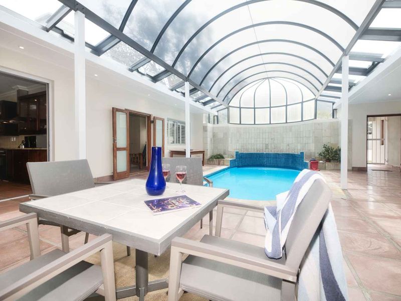 An indoor swimming pool area featuring a large retractable roof, tiled flooring, and direct access to the main living spaces.