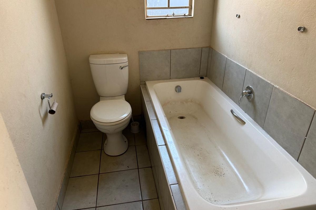 A dated bathroom featuring a standard bathtub and toilet with tiled splashbacks and flooring, requiring cosmetic updates and deep cleaning.