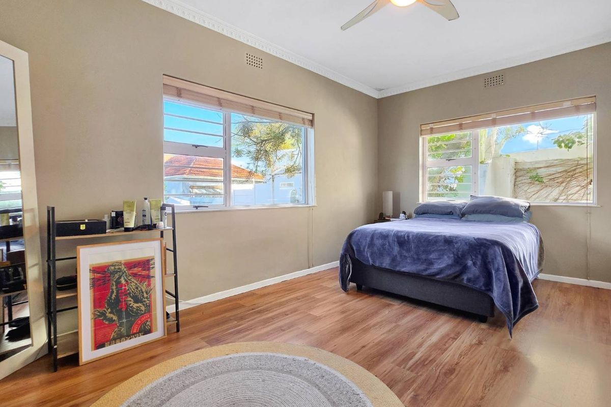 A well-lit bedroom featuring laminate flooring, ceiling fan, and large windows with security bars, offering a comfortable and functional living space.