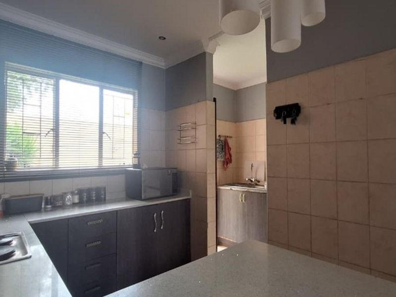 Functional kitchen featuring dark cabinetry, stone countertops, integrated hob, and a tiled splashback, with an adjoining scullery area.