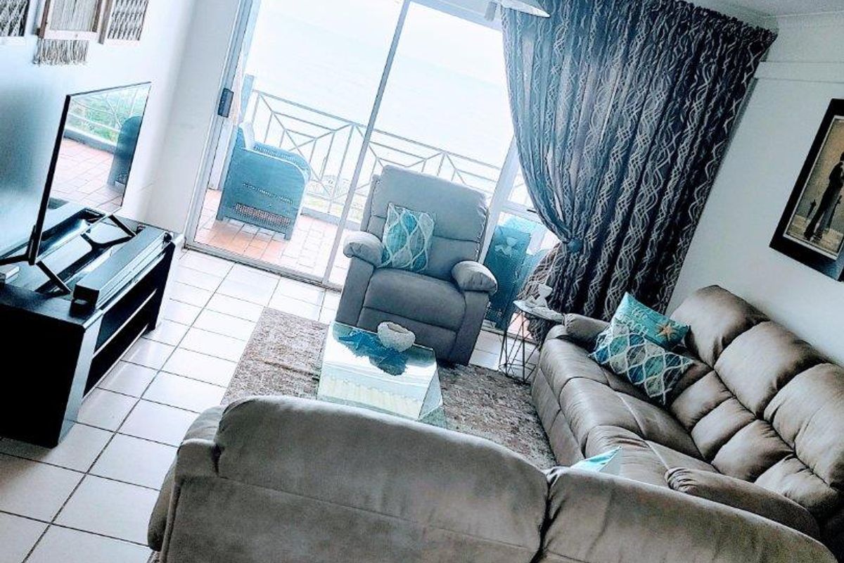 A living room featuring tiled flooring and large sliding glass doors that provide access to a balcony with ocean views.
