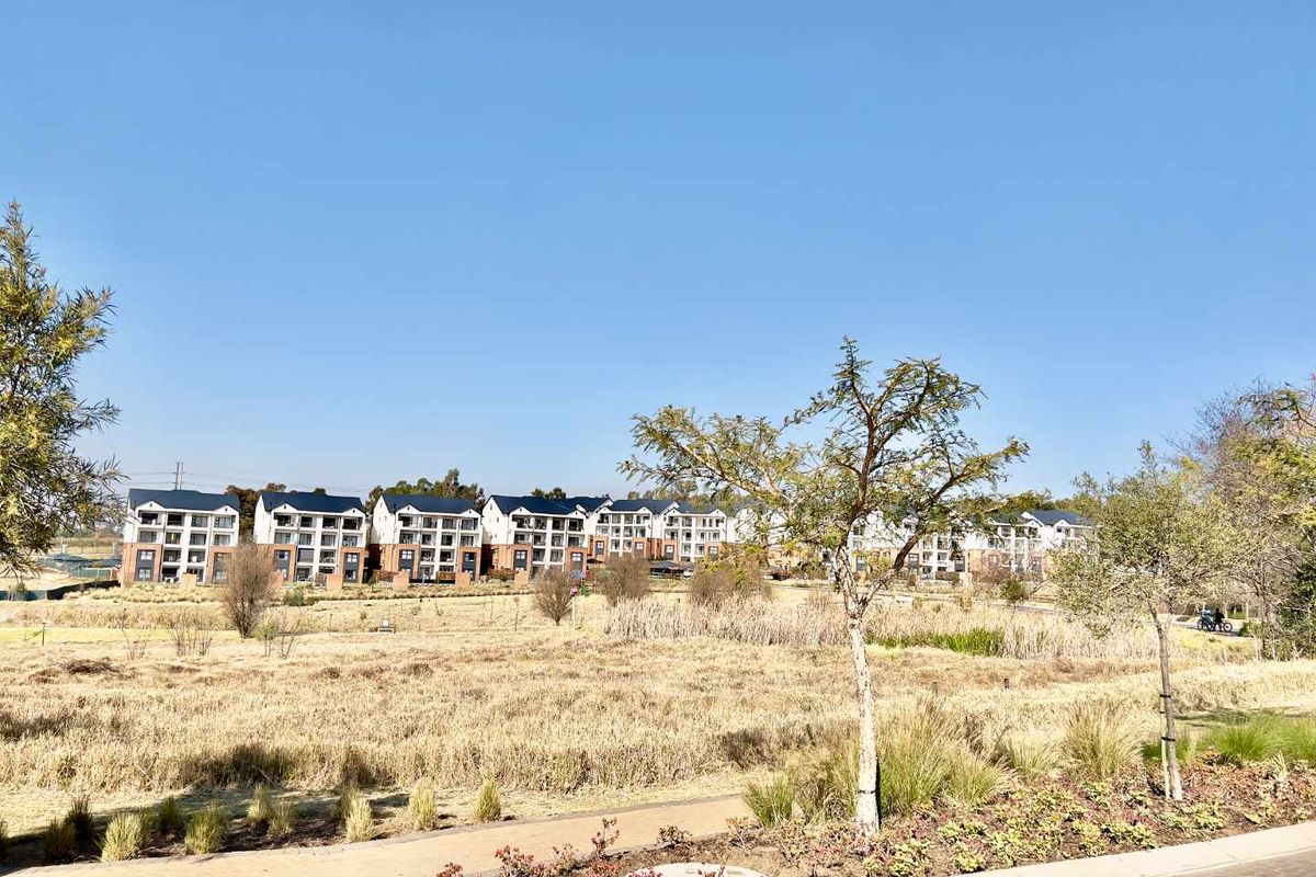 A wide-angle view of a modern apartment complex set within a landscaped estate, featuring paved walkways and natural vegetation.