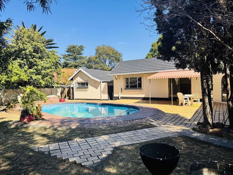 Rear exterior view featuring a swimming pool, paved patio area with an awning, and established garden surroundings.